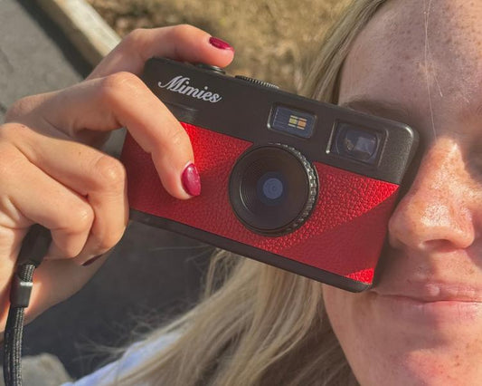 Woman holding the red Mimies screen-free digital camera up to her eye in the sun