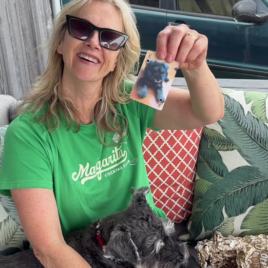 A mum holds up a playing card with a photo of her dog as a puppy, with the dog on her lap