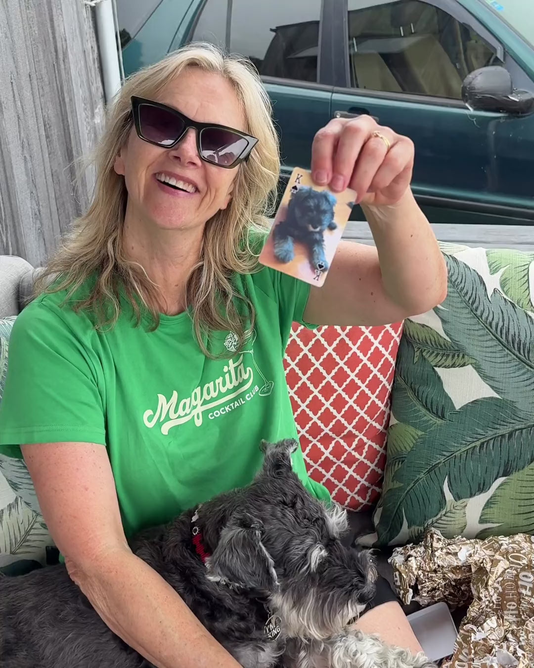 A mum holds up a playing card with a photo of her dog as a puppy, with the dog on her lap